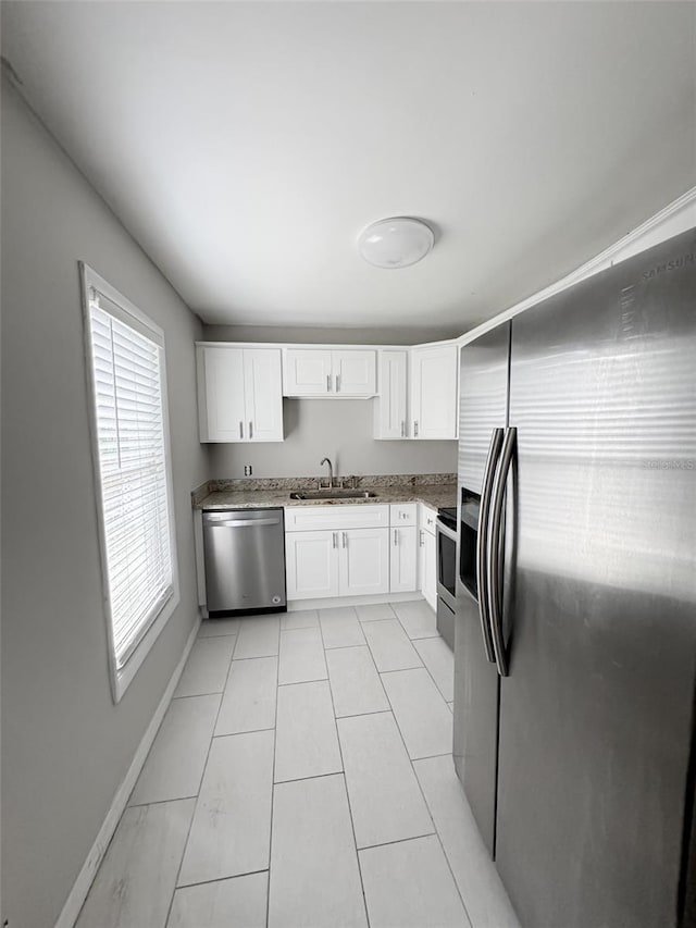 kitchen featuring appliances with stainless steel finishes, a sink, white cabinetry, and baseboards