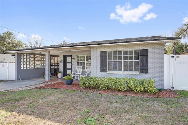 view of front of home with brick siding, an attached carport, a front lawn, fence, and concrete driveway