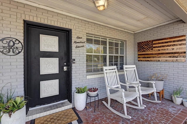 view of exterior entry with brick siding and covered porch