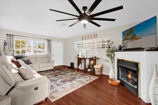 living room featuring visible vents, baseboards, wood finished floors, a glass covered fireplace, and a ceiling fan