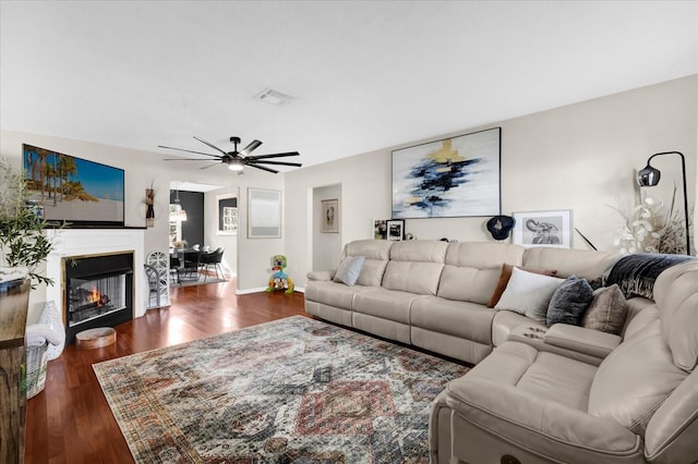 living area featuring visible vents, a glass covered fireplace, wood finished floors, baseboards, and ceiling fan