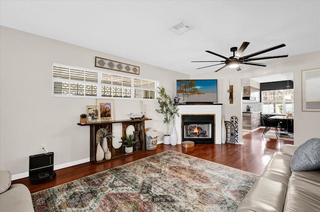 living room featuring a ceiling fan, baseboards, wood finished floors, visible vents, and a lit fireplace