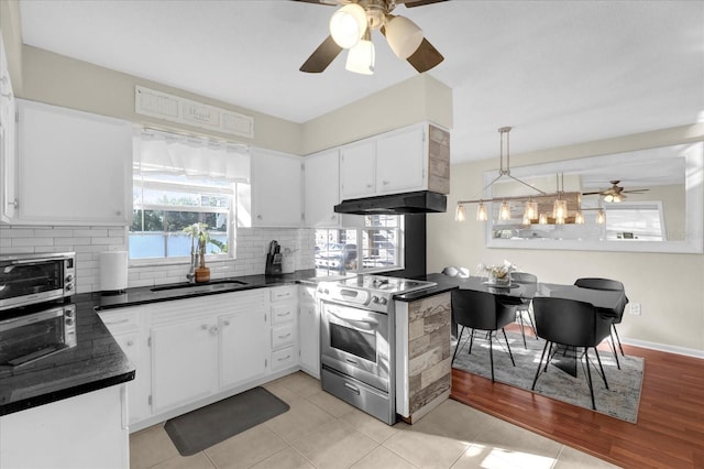 kitchen featuring dark countertops, under cabinet range hood, stainless steel electric range oven, decorative backsplash, and a sink