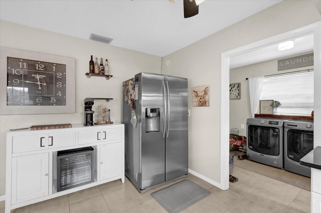 kitchen with light tile patterned floors, visible vents, white cabinetry, washing machine and dryer, and stainless steel fridge