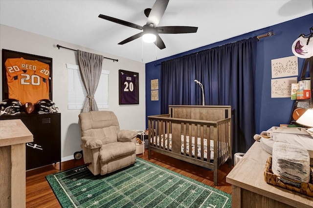 bedroom featuring baseboards, a crib, a ceiling fan, and wood finished floors