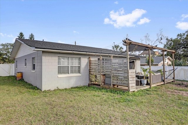 back of house featuring concrete block siding, a lawn, fence, and a shingled roof