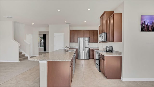 kitchen with brown cabinets, an island with sink, recessed lighting, appliances with stainless steel finishes, and light stone countertops