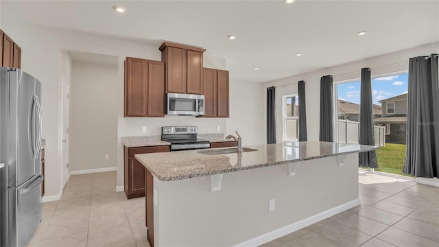 kitchen featuring light stone countertops, an island with sink, recessed lighting, a sink, and stainless steel appliances