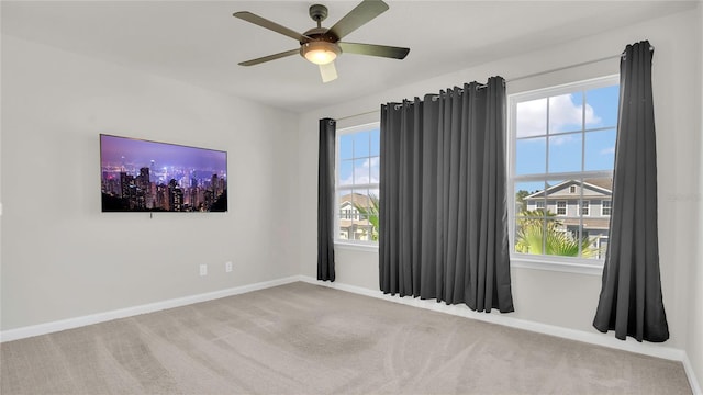 carpeted spare room with a wealth of natural light, baseboards, and a ceiling fan