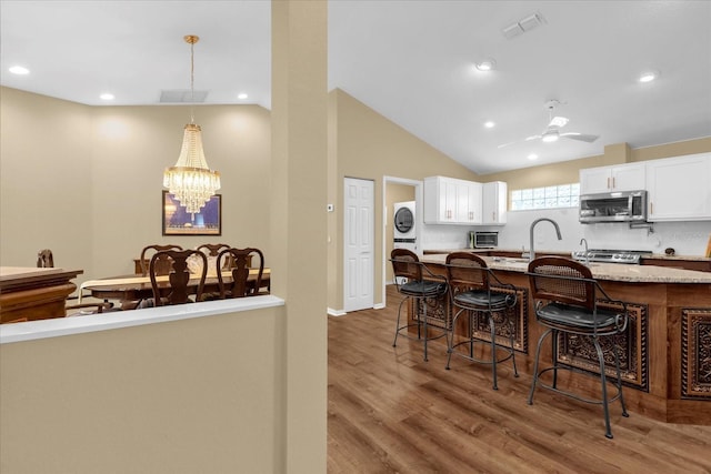 kitchen featuring a breakfast bar area, stacked washer / drying machine, stainless steel microwave, white cabinets, and wood finished floors