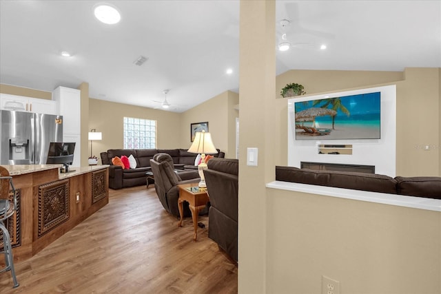 living area with vaulted ceiling, light wood-type flooring, visible vents, and a ceiling fan