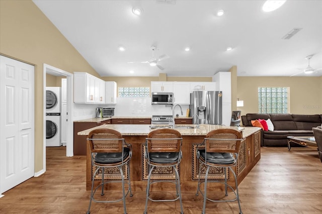 kitchen featuring stacked washer and clothes dryer, a ceiling fan, appliances with stainless steel finishes, lofted ceiling, and a sink