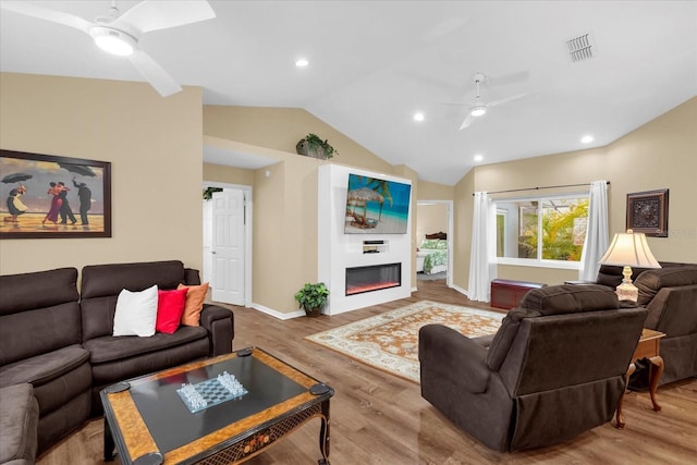 living area with visible vents, ceiling fan, wood finished floors, lofted ceiling, and a glass covered fireplace