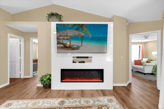 living room with vaulted ceiling, wood finished floors, ceiling fan, and a glass covered fireplace