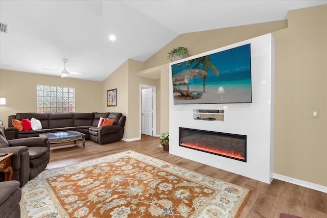living area with lofted ceiling, baseboards, visible vents, a glass covered fireplace, and wood finished floors