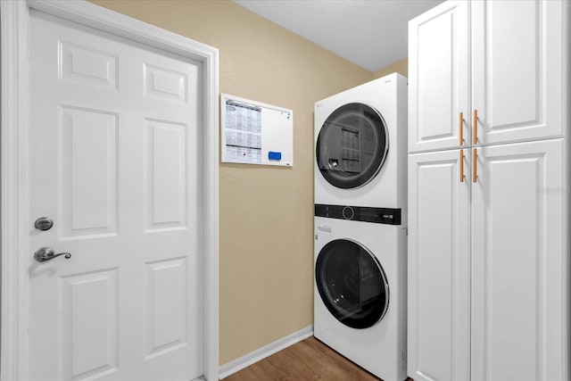 clothes washing area with cabinet space, baseboards, stacked washing maching and dryer, and wood finished floors