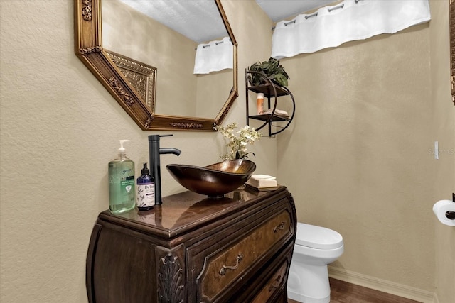 bathroom with baseboards, toilet, wood finished floors, vanity, and a textured wall