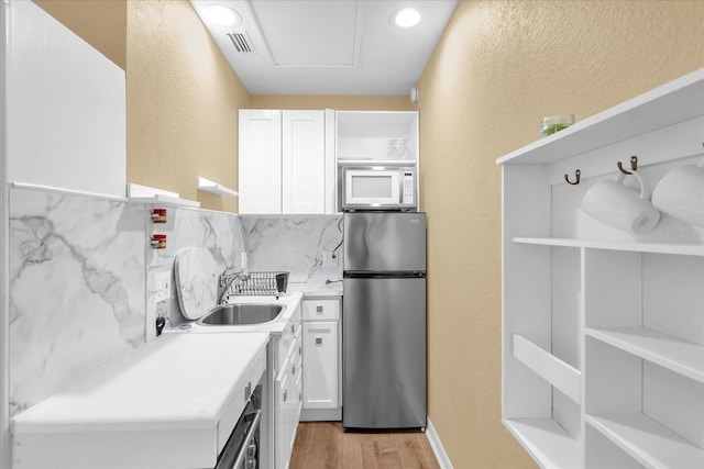 kitchen featuring white cabinetry, open shelves, a sink, freestanding refrigerator, and white microwave