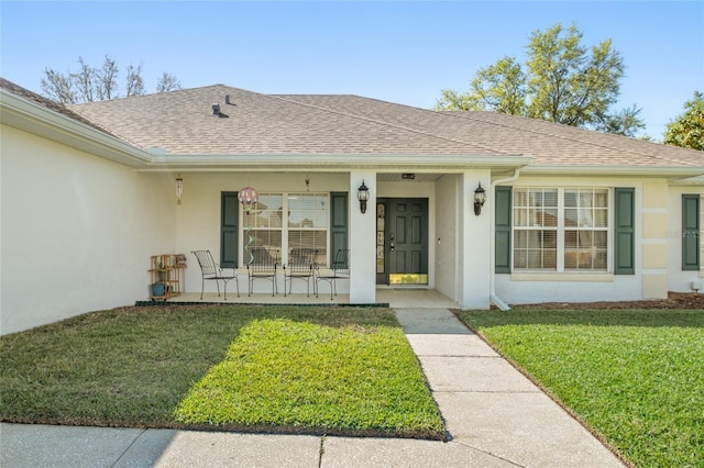 property entrance with stucco siding, a porch, a shingled roof, and a lawn