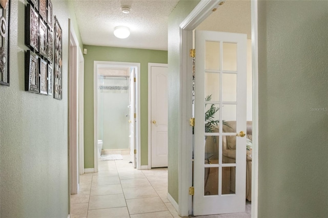 hall with light tile patterned floors, a textured ceiling, baseboards, and a textured wall