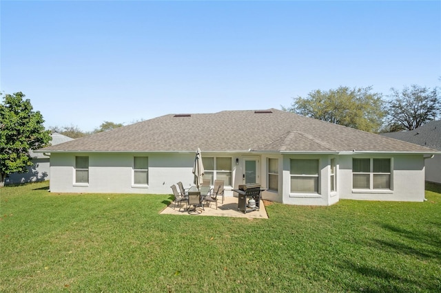 rear view of house with stucco siding, a lawn, a patio, and roof with shingles