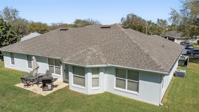 back of house featuring roof with shingles, central AC unit, a lawn, stucco siding, and a patio area