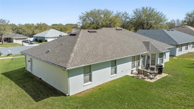 back of property with a lawn, a patio area, stucco siding, and a shingled roof