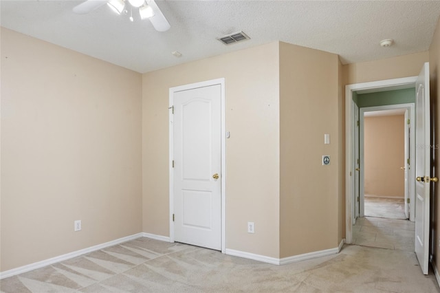 empty room featuring a textured ceiling, visible vents, baseboards, ceiling fan, and light carpet