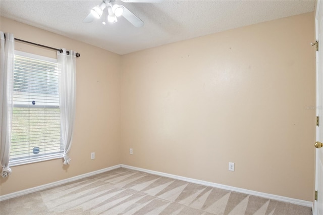 spare room with light colored carpet, a textured ceiling, baseboards, and a ceiling fan