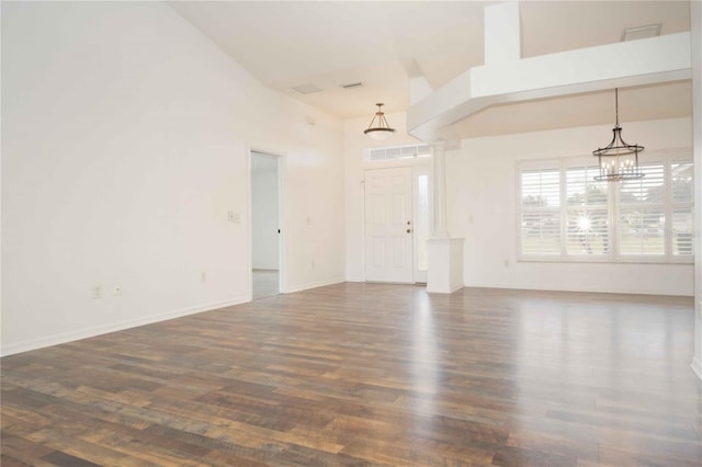 empty room with an inviting chandelier, dark wood-type flooring, baseboards, and a towering ceiling