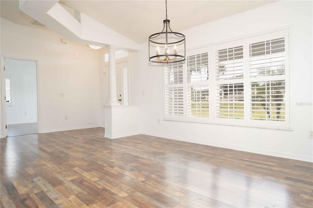 empty room featuring a notable chandelier, lofted ceiling, ornate columns, and wood finished floors