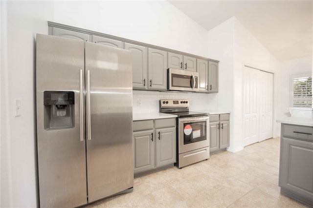 kitchen featuring light countertops, lofted ceiling, decorative backsplash, gray cabinets, and stainless steel appliances