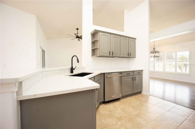 kitchen with gray cabinets, ceiling fan with notable chandelier, a sink, open shelves, and stainless steel dishwasher