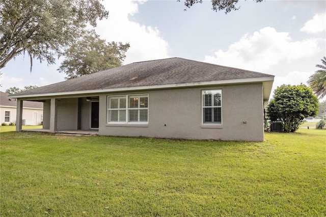 rear view of house featuring a yard, a patio area, a shingled roof, and stucco siding