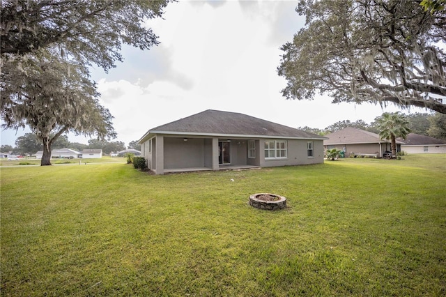 back of house featuring a lawn, an outdoor fire pit, and stucco siding