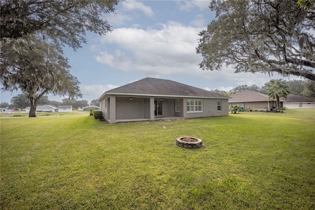 rear view of property featuring stucco siding, a fire pit, and a yard