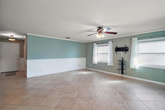 empty room featuring light tile patterned floors, a wainscoted wall, ceiling fan, and ornamental molding