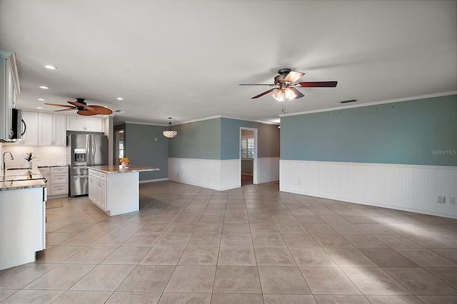 kitchen featuring open floor plan, wainscoting, appliances with stainless steel finishes, and white cabinetry