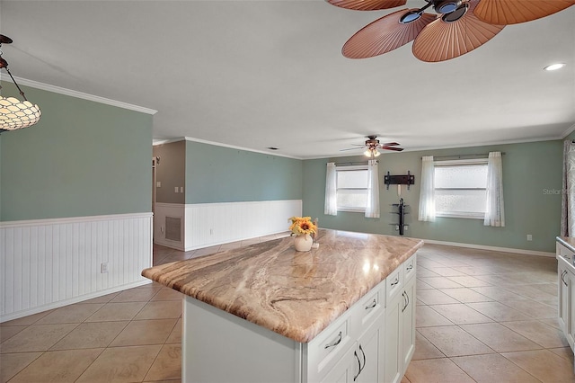 kitchen with ornamental molding, a center island, white cabinetry, wainscoting, and light tile patterned floors