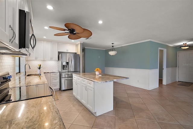 kitchen featuring a wainscoted wall, stainless steel appliances, light tile patterned flooring, white cabinetry, and a sink