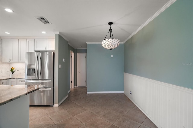 kitchen with light stone counters, visible vents, ornamental molding, white cabinetry, and stainless steel fridge