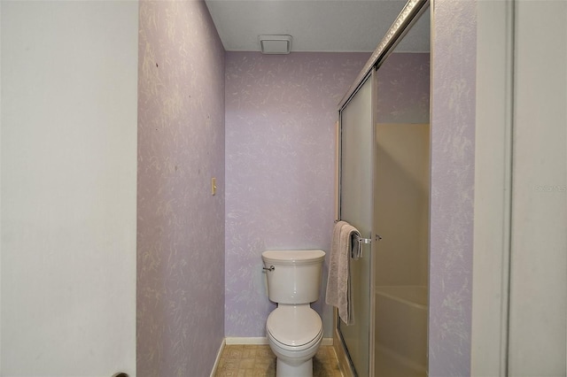 bathroom featuring a shower with door, toilet, baseboards, and a textured wall