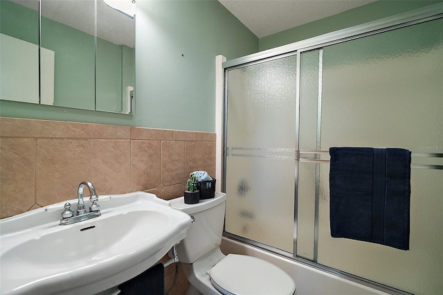 full bath featuring a wainscoted wall, toilet, a textured ceiling, tile walls, and bath / shower combo with glass door