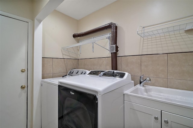 laundry room with a sink, tile walls, cabinet space, and washer and clothes dryer