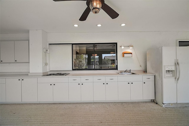 kitchen with a sink, cooktop, light countertops, white cabinets, and white refrigerator with ice dispenser