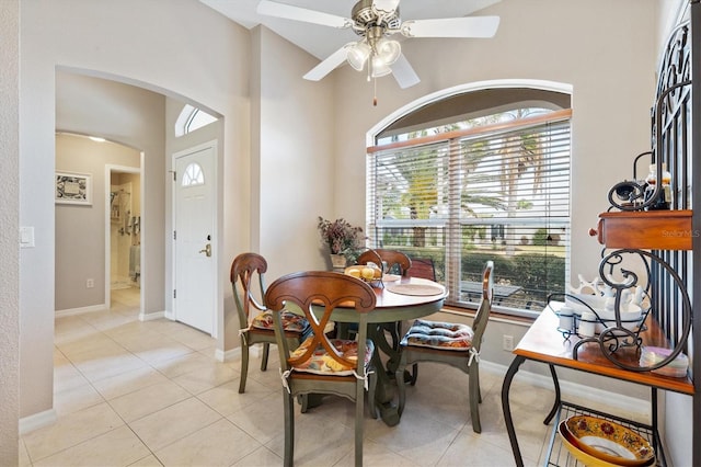 dining area with baseboards, arched walkways, light tile patterned flooring, and a ceiling fan