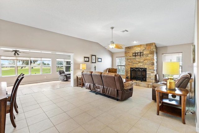 living area with light tile patterned floors, a stone fireplace, a ceiling fan, and vaulted ceiling