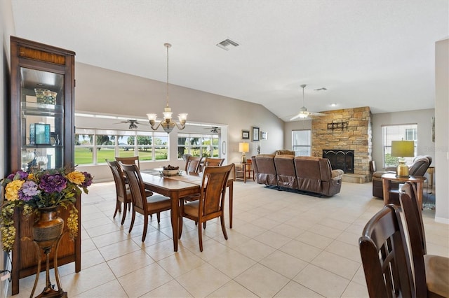 dining area with a stone fireplace, lofted ceiling, ceiling fan with notable chandelier, and visible vents