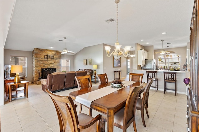 dining room featuring light tile patterned floors, a stone fireplace, and ceiling fan with notable chandelier