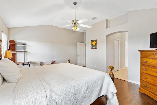 bedroom featuring visible vents, lofted ceiling, wood finished floors, arched walkways, and a ceiling fan